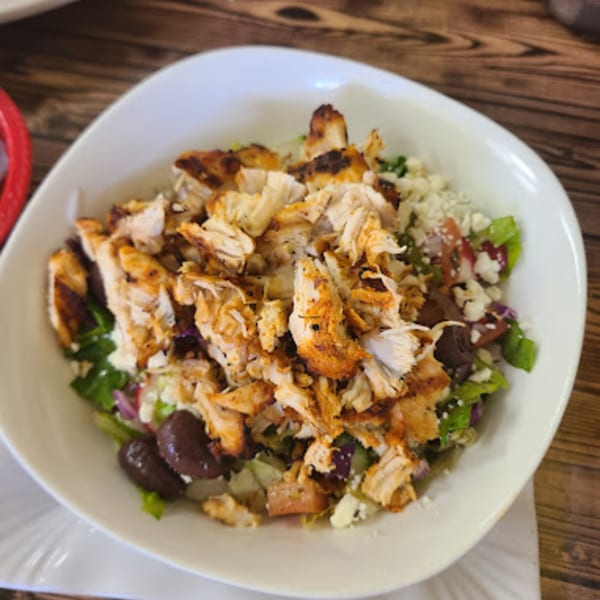 A white bowl of Habibi's Cafe & Pizzeria's chicken salad with olives, feta, and greens.
