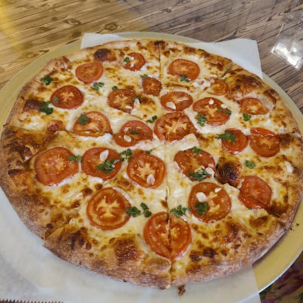 Habibi's Cafe & Pizzeria's whole pizza with sliced tomatoes, cheese, and green herbs on a wooden table.