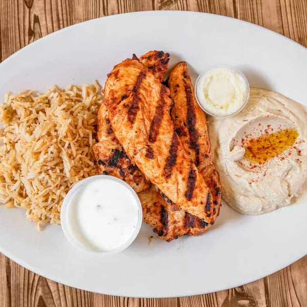 Grilled chicken breast with rice, hummus, and two dipping sauces on a white plate.